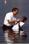 A man lowers a boy into a body of water in order to baptize him by immersion